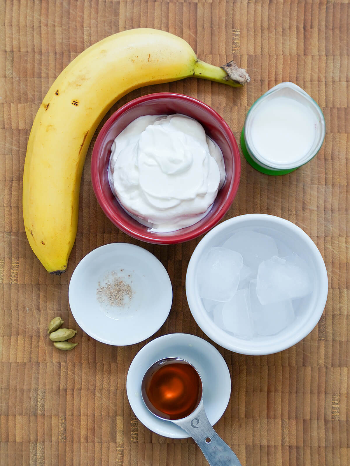 bowls of yogurt, ice, measure of milk, honey with banana to side and cardamon pods.