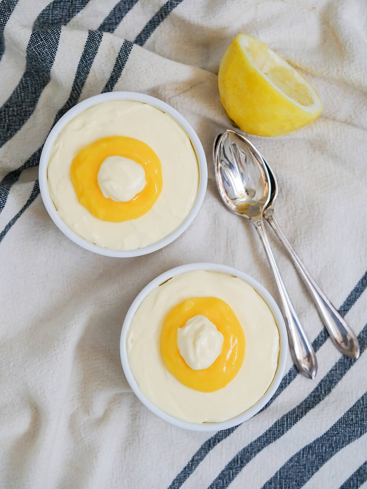 overhead view of two dishes of lemon mousse topped with extra lemon curd in middle, spoons to side of dishes.