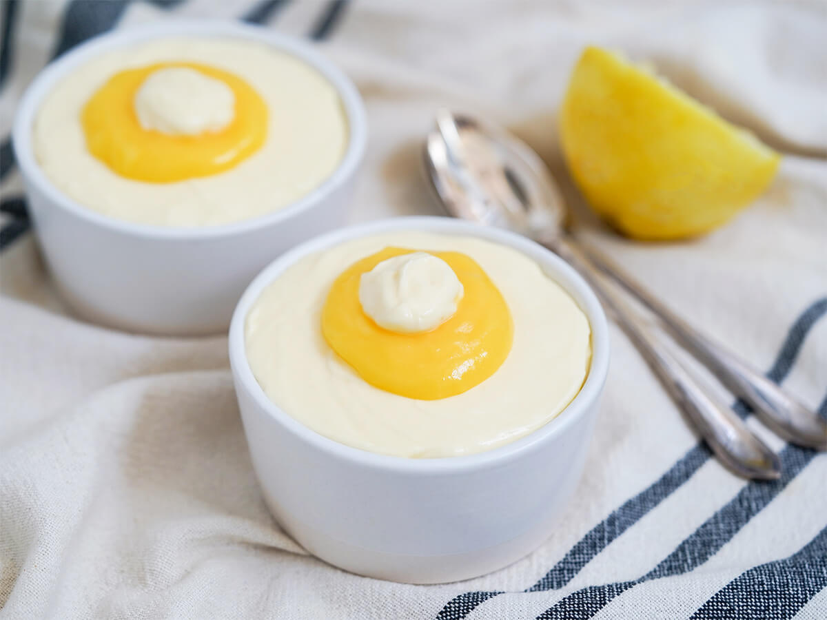 two dishes of lemon mousse with half lemon and spoons blurred in side background.
