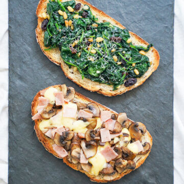two llescas Catalan loaded toasts above each other, one with spinach topping other with ham, cheese and mushrooms.