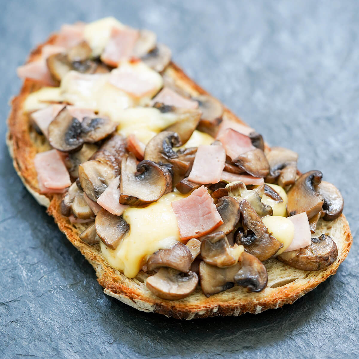 llescas Catalan bread pizza toast topped with mushrooms, ham and cheese, with cheese melting into rest.