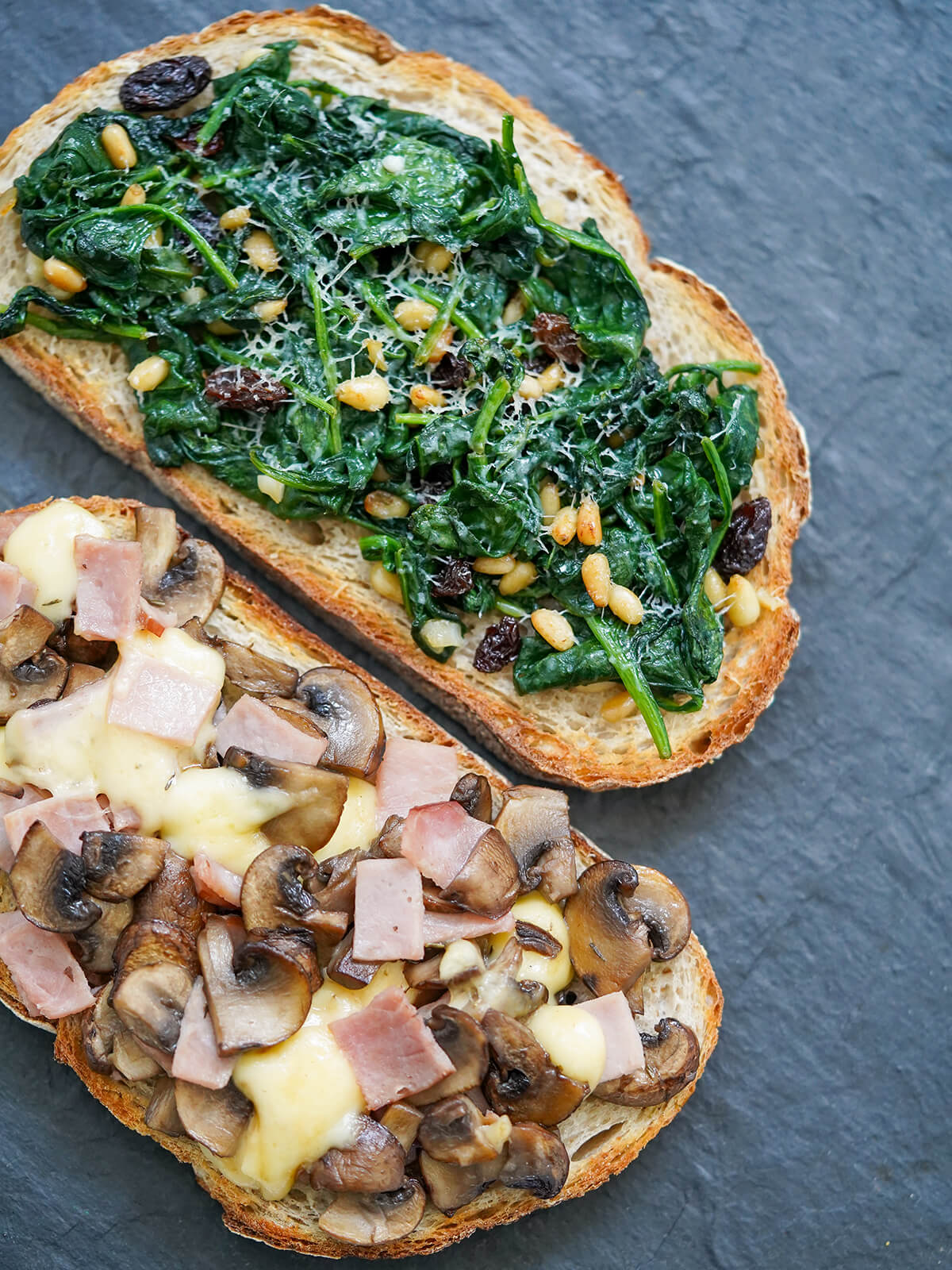 Llescas are Catalan loaded toasts that can have a whole range of toppings. These classics - spinach, pine nuts & raisins, and ham, mushroom & cheese - are tasty, quick and easy to make. Great as a snack or easy meal. overhead part view of two llescas, Catalan loaded toasts, one topped with spinach other ham, mushroom and cheese.