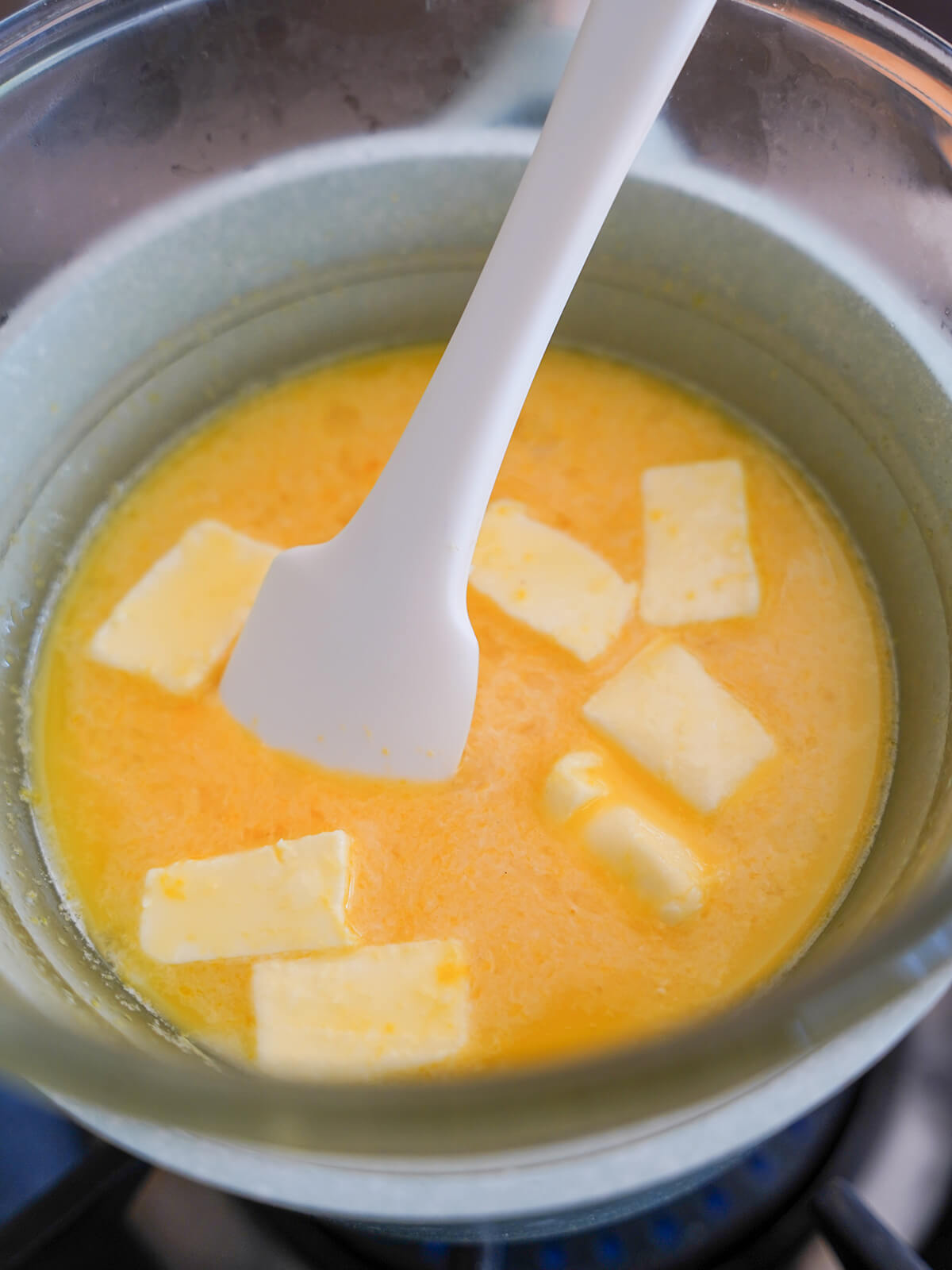 stirring mixture of egg and lemon with chunks of butter in it in bowl over water on stove.