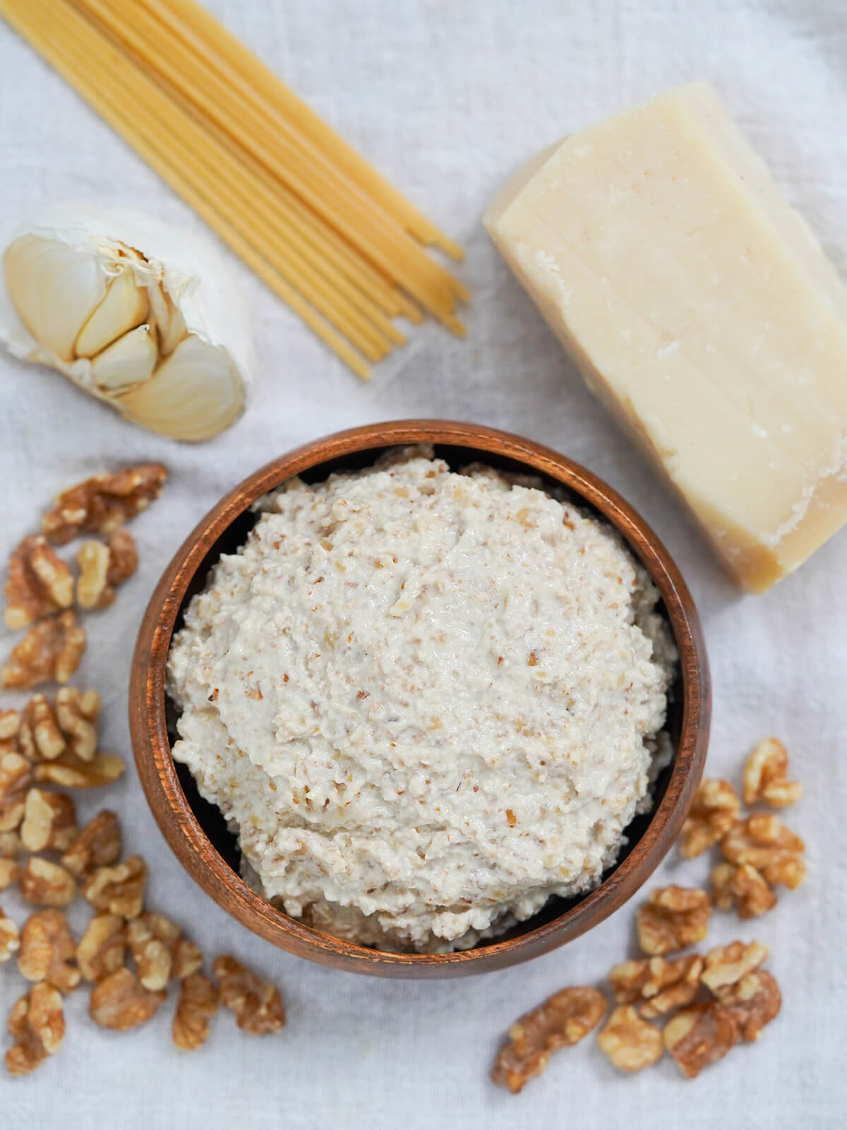 overhead view of a dish of walnut sauce, salsa di noci, with nuts, cheese, spaghetti and garlic around bowl.