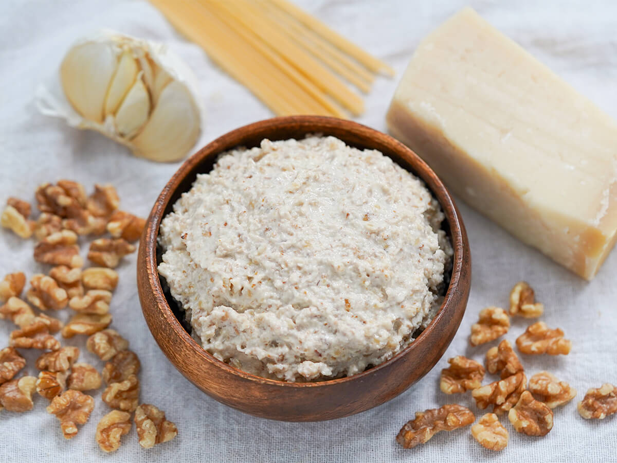 dish of walnut sauce, salsa di noci, with walnut pieces, garlic, cheese and pasta around bowl.