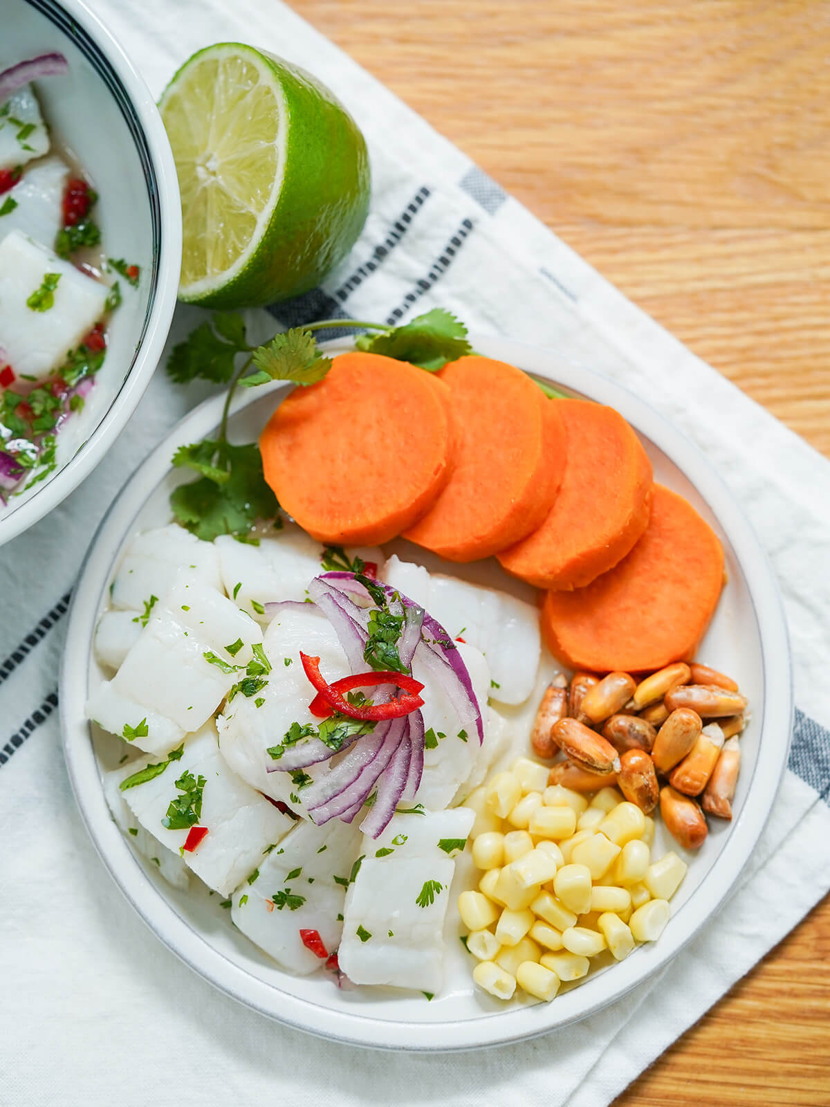overhead view of a plate of Peruvian ceviche with slices of sweet potato, corn and fried corn, with lime above plate on cloth.