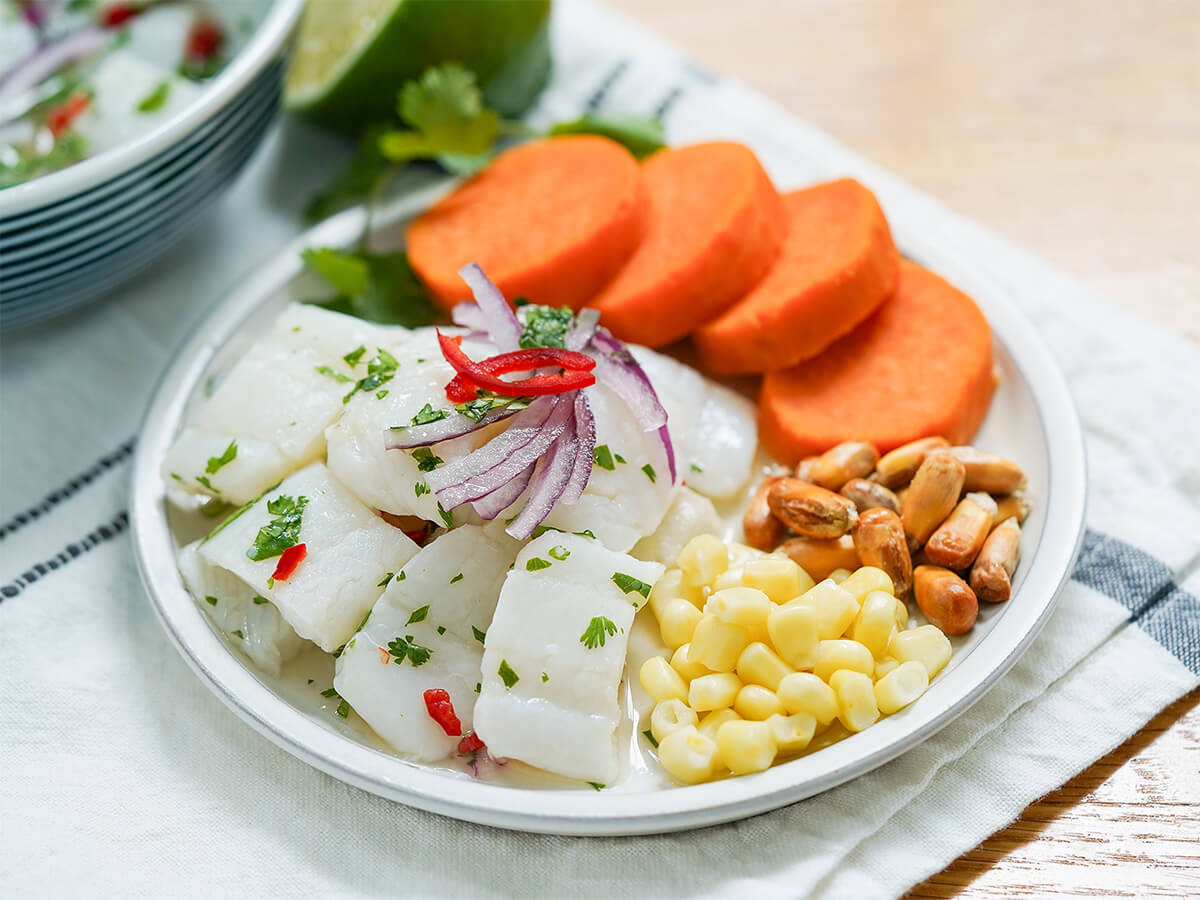 side view of plate with Peruvian ceviche, slices of sweet potato and corn with red onion slices on top of the fish.