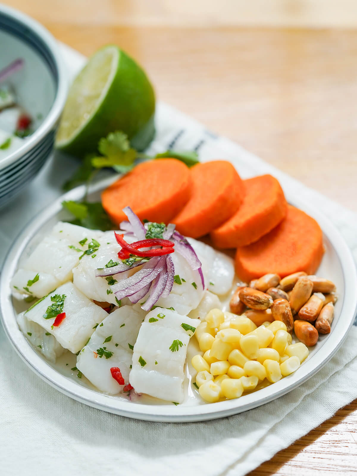 plate of Peruvian ceviche with corn to side and sliced sweet potato behind on plate, half lime in background.