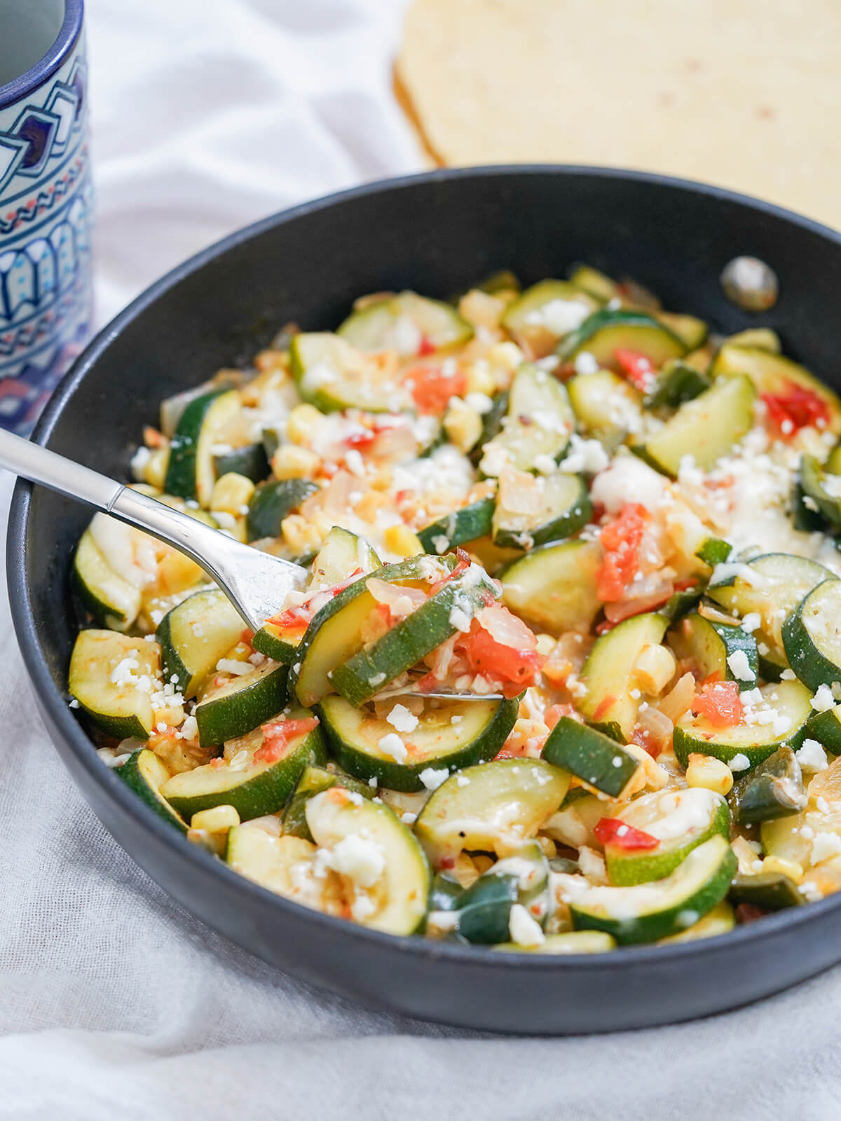 Calabacitas is an easy and delicious Mexican zucchini dish, with corn, tomato and cheese. It's quick, fresh yet comforting and perfect as a side dish, taco filling or vegetarian main. side view of skillet of calabacitas, Mexican zucchini with fork resting on top.