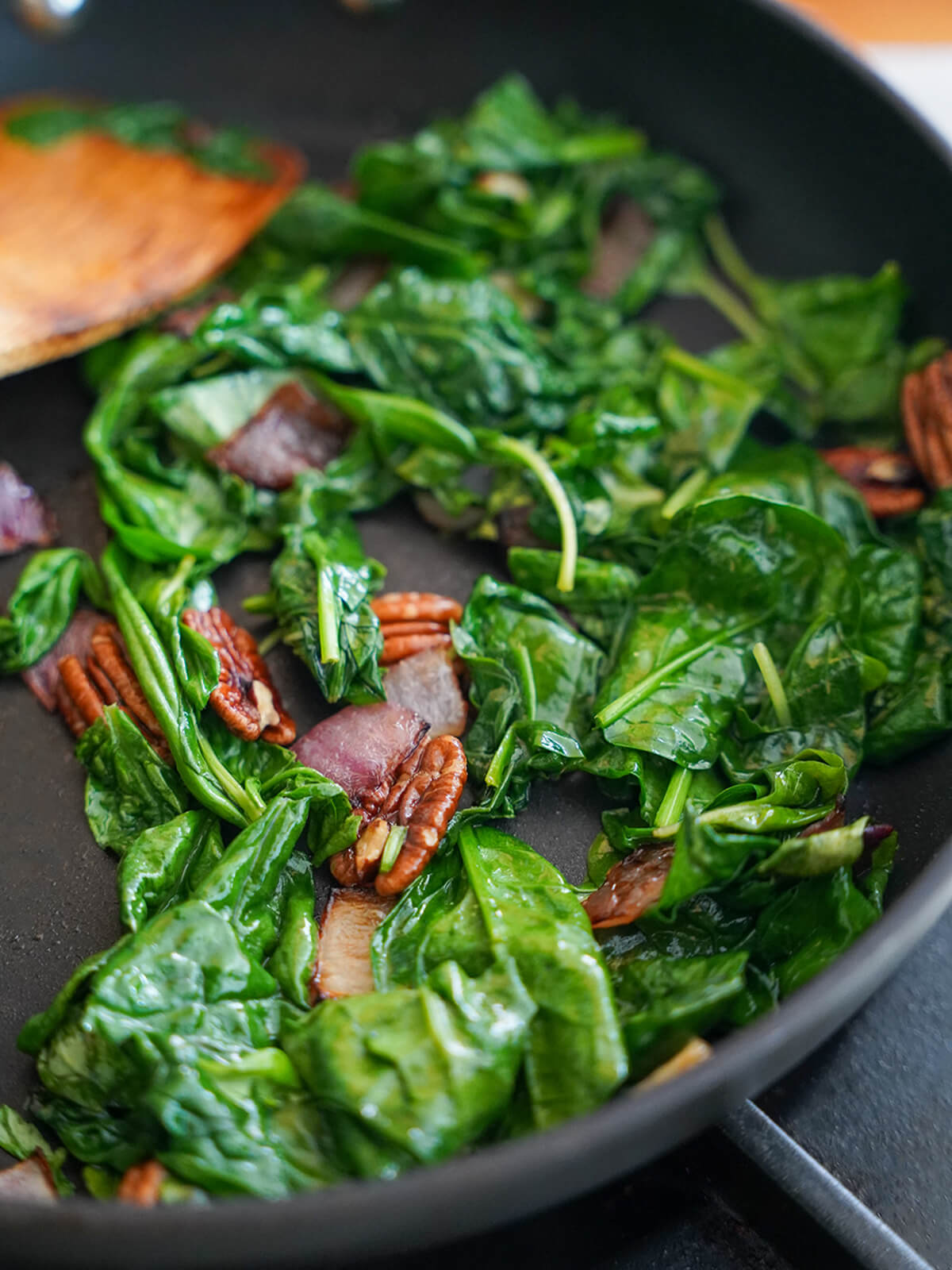 wilting spinach and basil in skillet with pecans, onion.