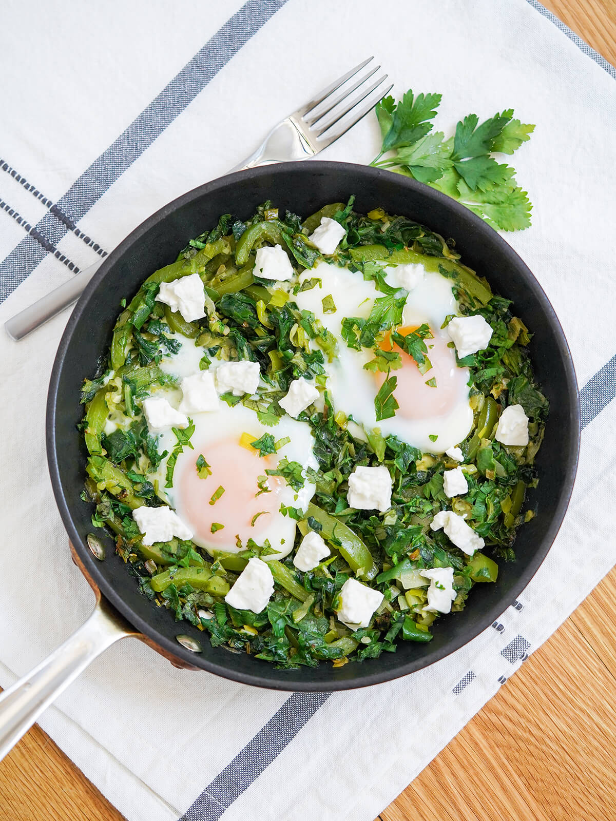 overhead view of skillet of green shakshuka with fork above.