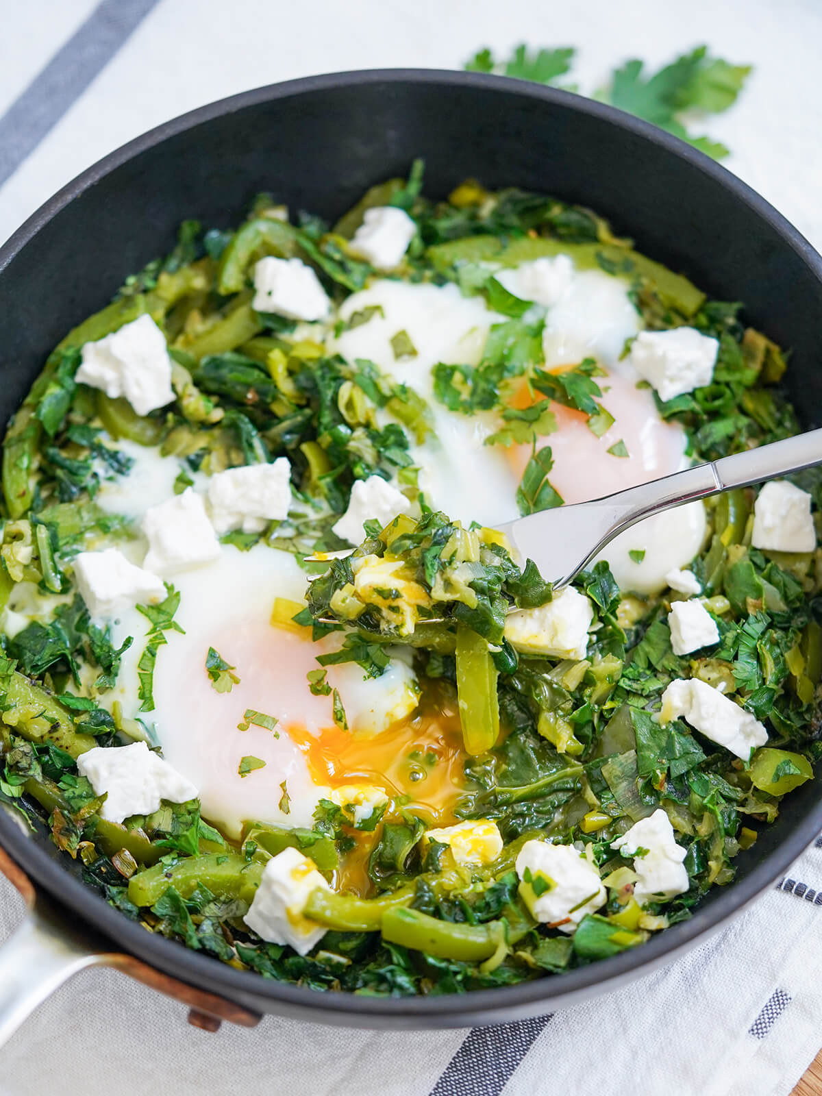 forkful of green shakshuka mixture resting in skillet showing runny yolk underneath.