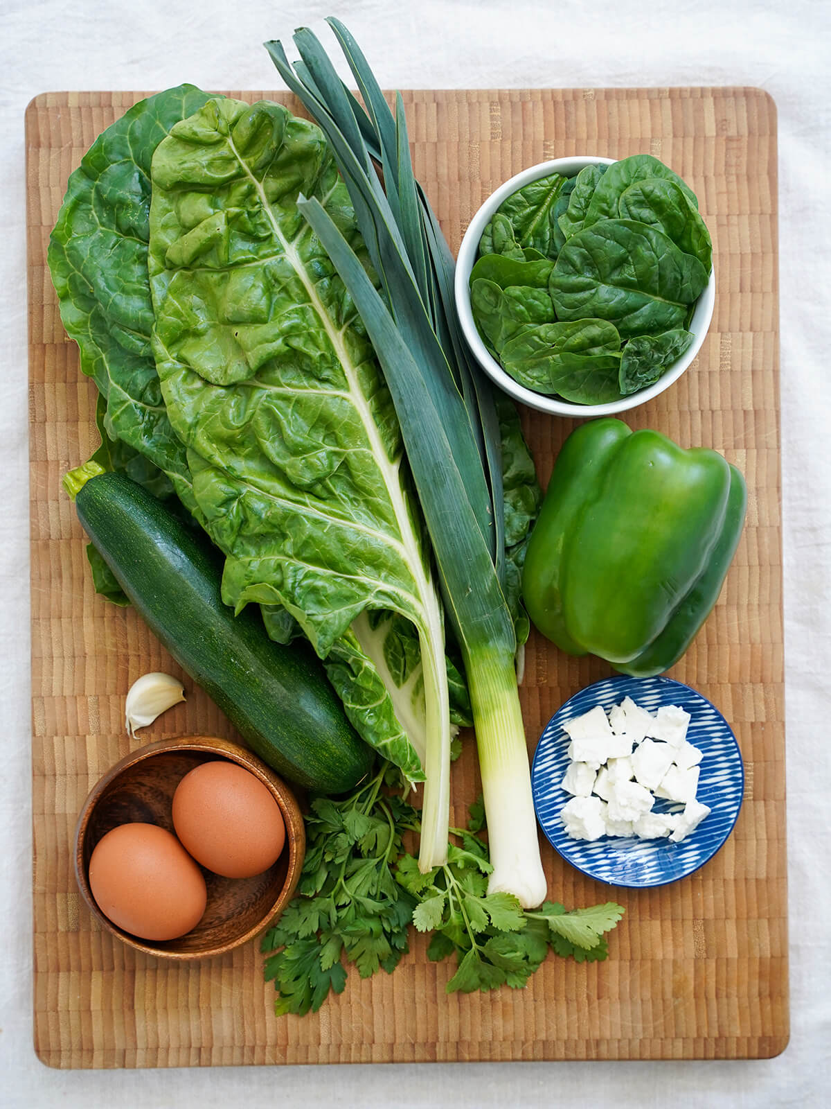 chard leaves, leek, zucchini, green pepper and bowls of spinach, eggs, feta on board.
