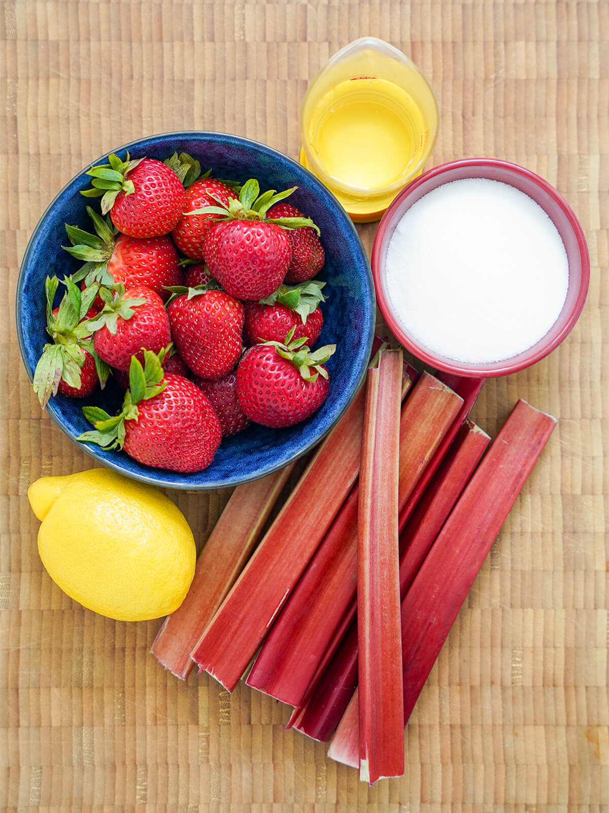 bowl of strawberries, stems of rhubarb, bowl of sugar, lemon and measure of water.