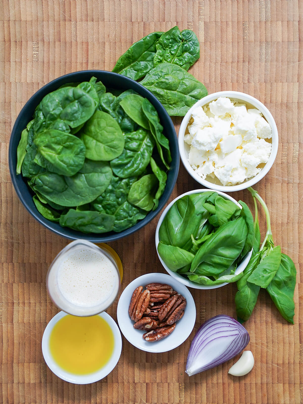 bowls of spinach, cheese, basil, pecans and measure of evaporated milk, oil, part of an onion and garlic clove.