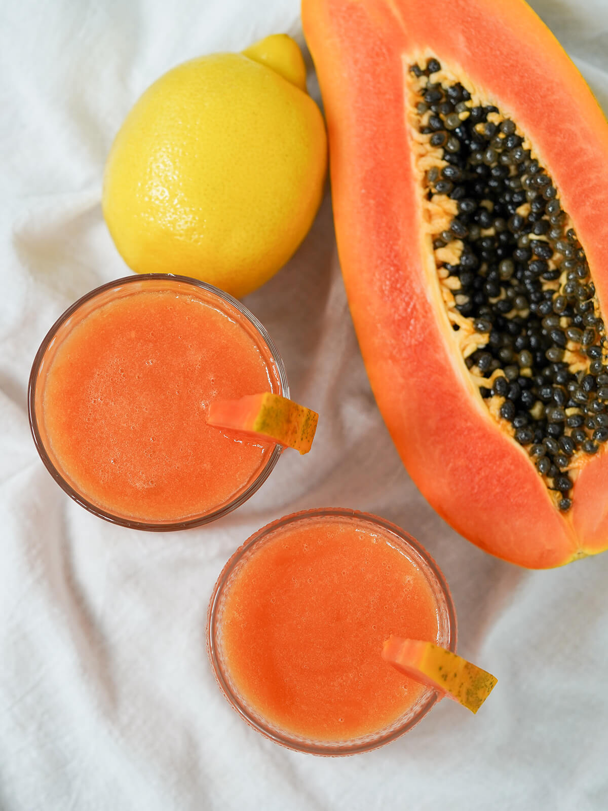 overhead view of two glasses of papaya lemonade with half papaya and lemon to side.