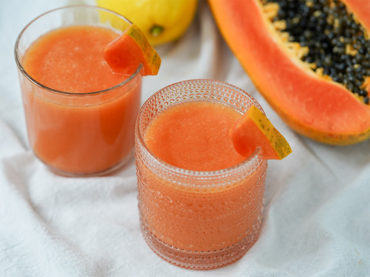 two glasses of papaya lemonade with part of a papaya in background.