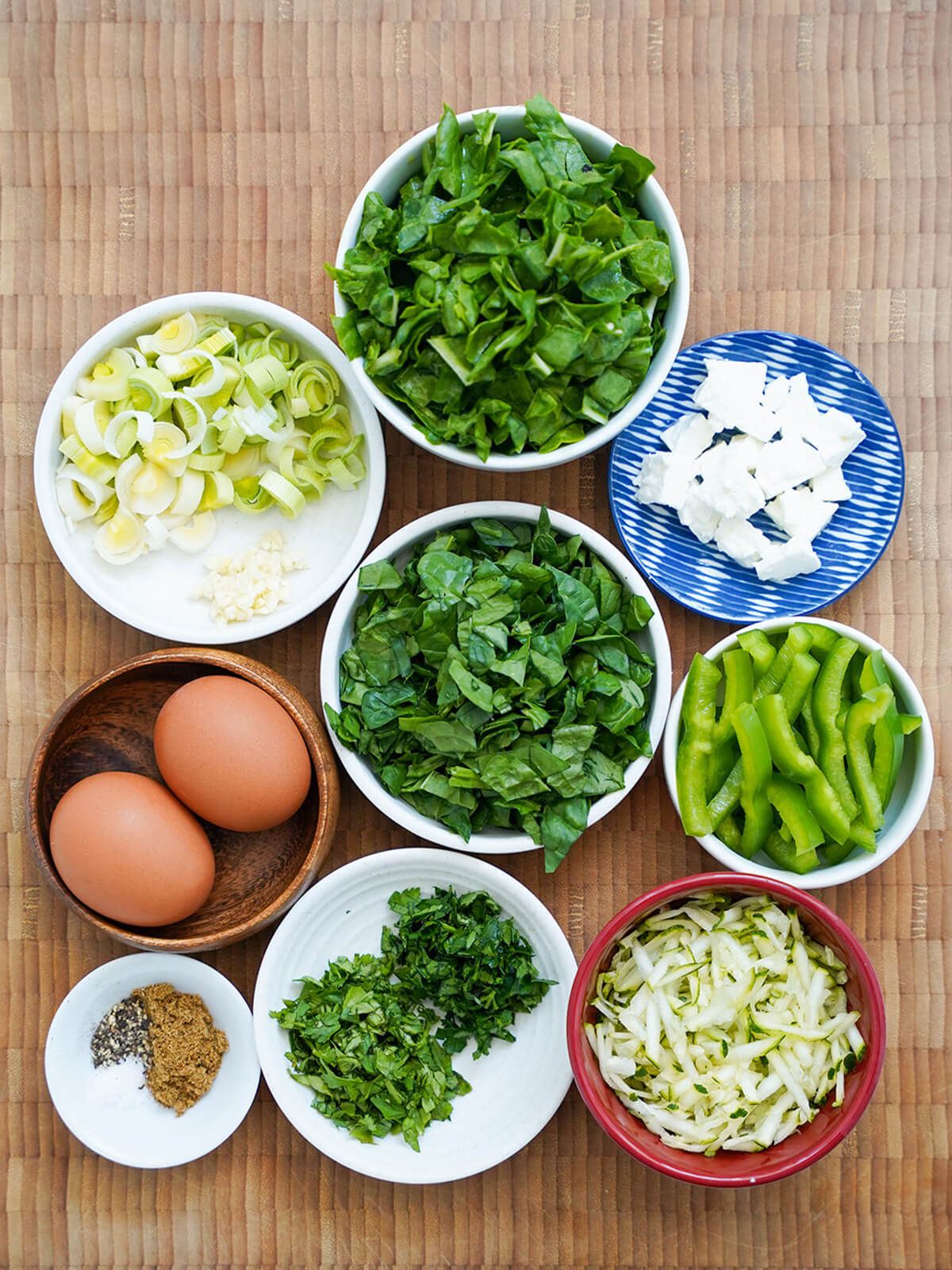 bowls of chopped chard, spinach, green pepper, leeks, grated zucchini, eggs and diced feta and chopped herbs.