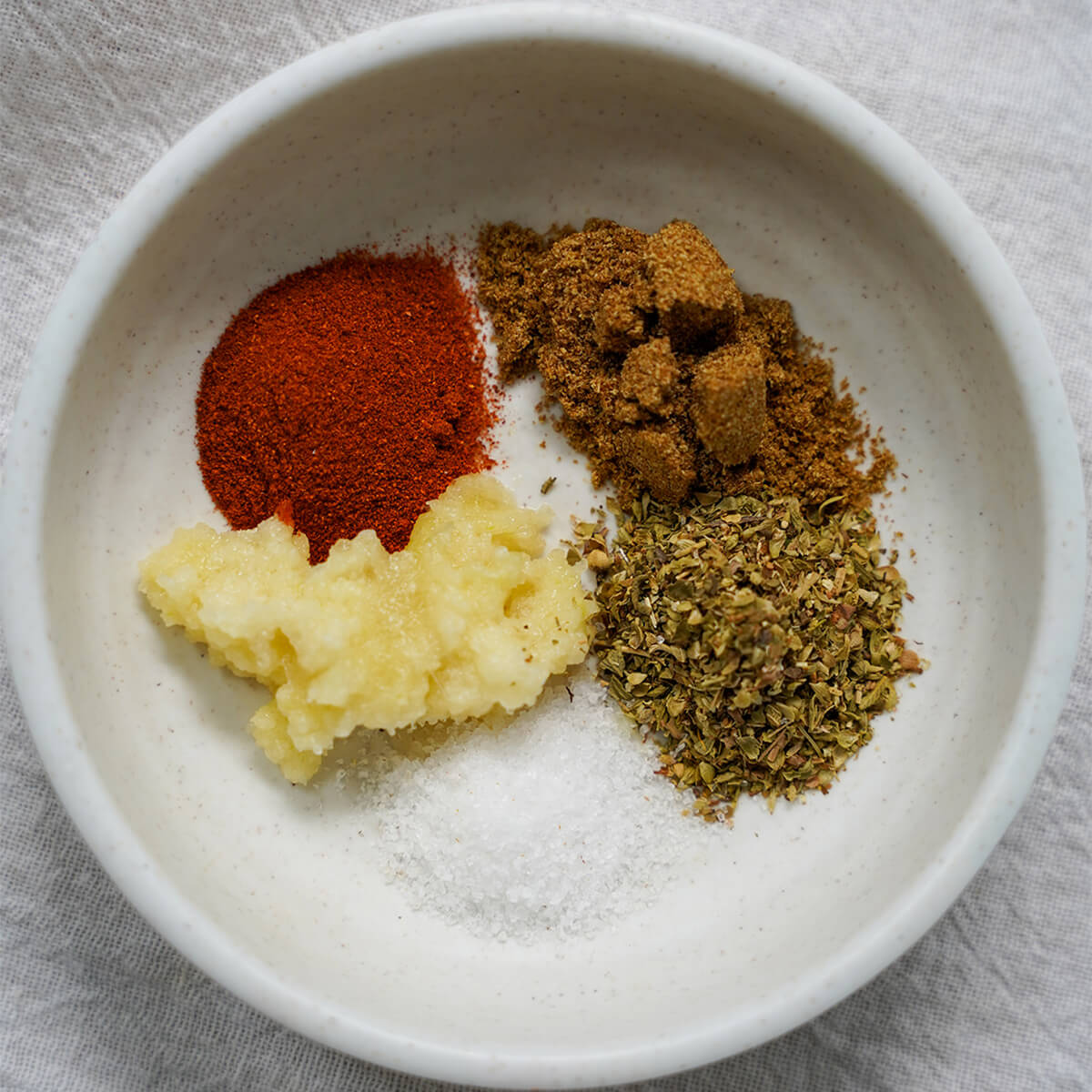 spices for pork carnitas dish with crushed garlic, salt, oregano, cumin and parika.