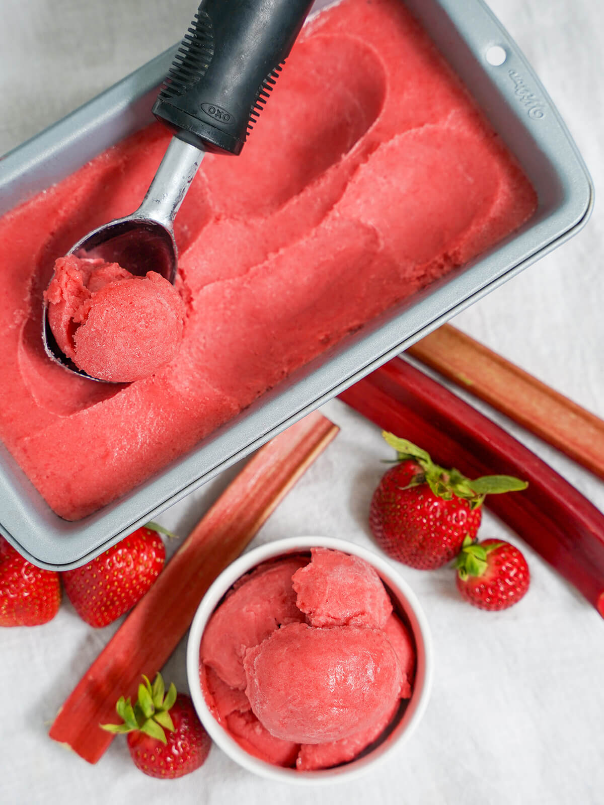 overhead view of small bowl of strawberry rhubarb sorbet and loaf tin with more in it and scoop on top.