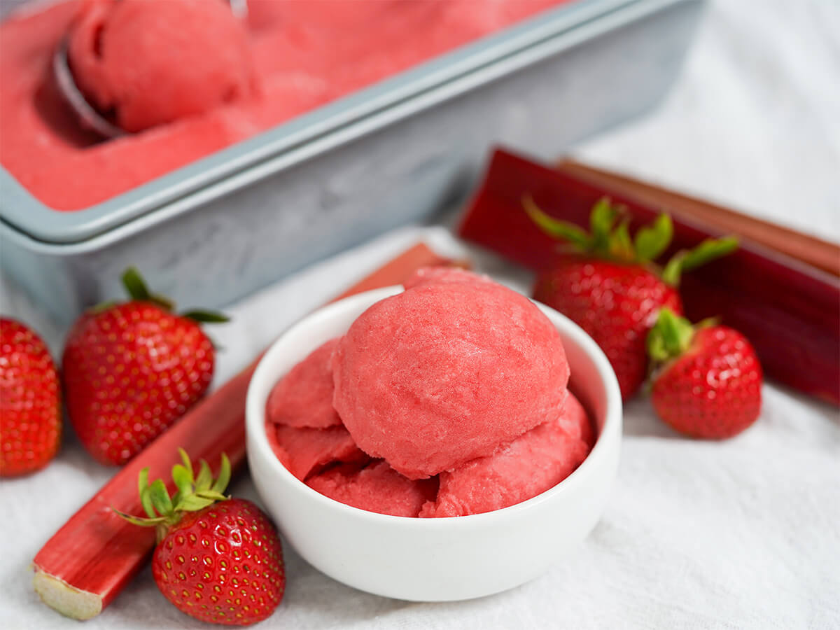bowl of strawberry rhubarb sorbet with strawberries and rhubarb stems either side.