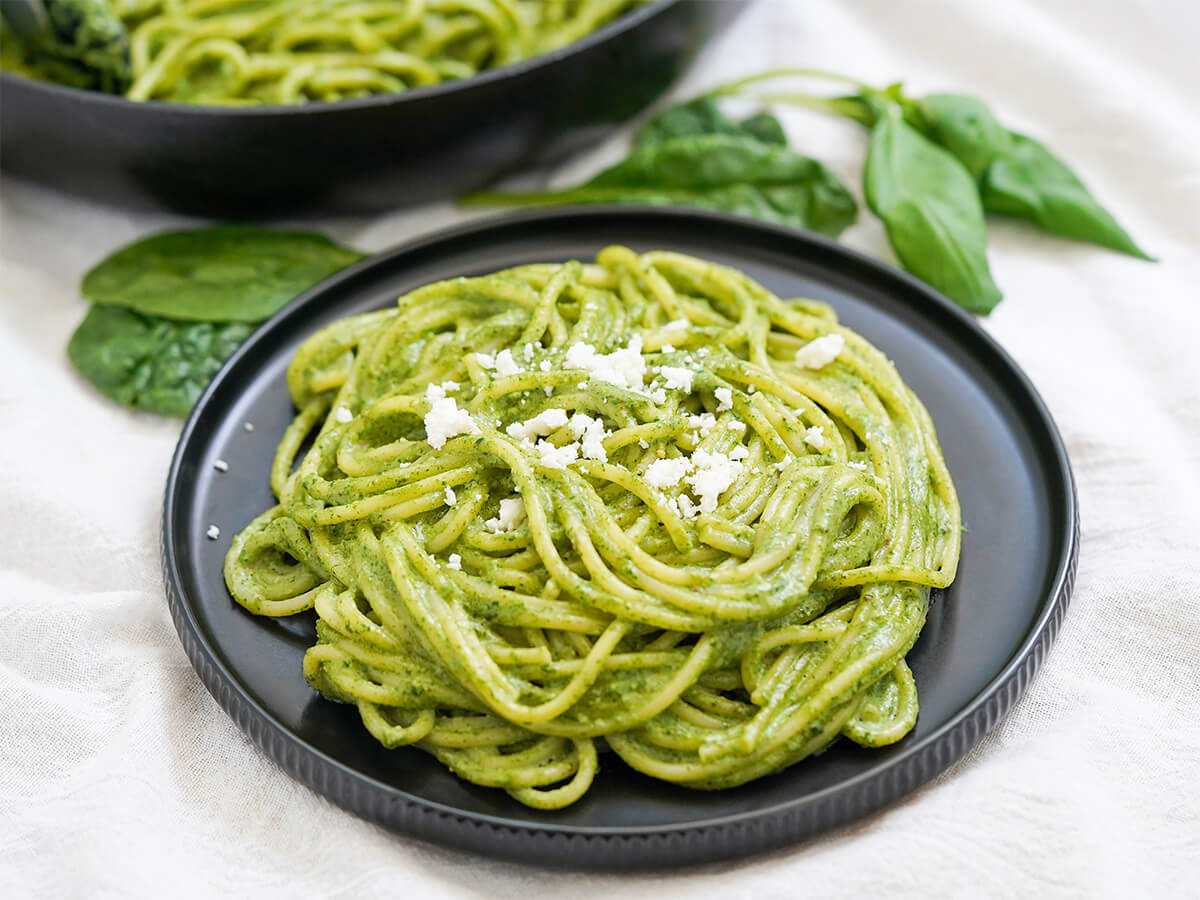 plate of tallarines verdes, pasta with Peruvian pesto, with spinach and basil leaves behind.