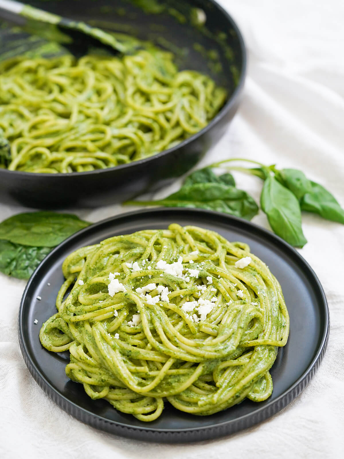 plate of tallarines verdes, pasta with Peruvian pesto, with skillet with more behind.