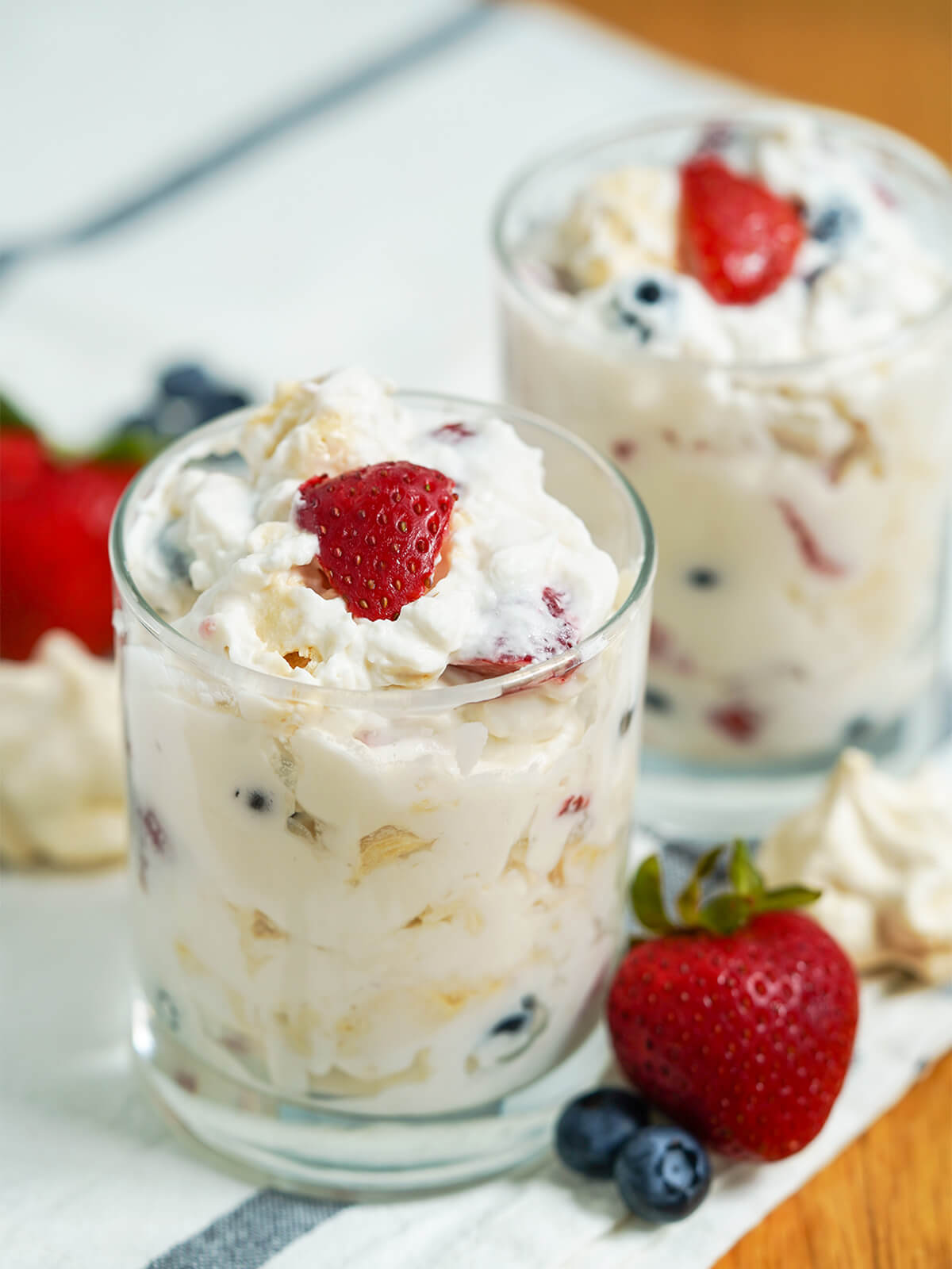 Eton mess is a classic British dessert that is incredibly easy to prepare - simply fruit, cream and meringue - but the result is a delicious treat whenever you enjoy it. two glasses of Eton mess with berries and meringue to side.