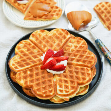 Plate of two Norwegian waffles stacked on top of each other with cream and sliced strawberries on top.