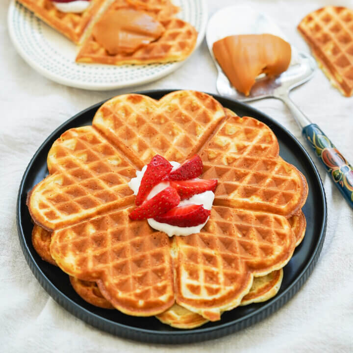 Plate of two Norwegian waffles stacked on top of each other with cream and sliced strawberries on top.