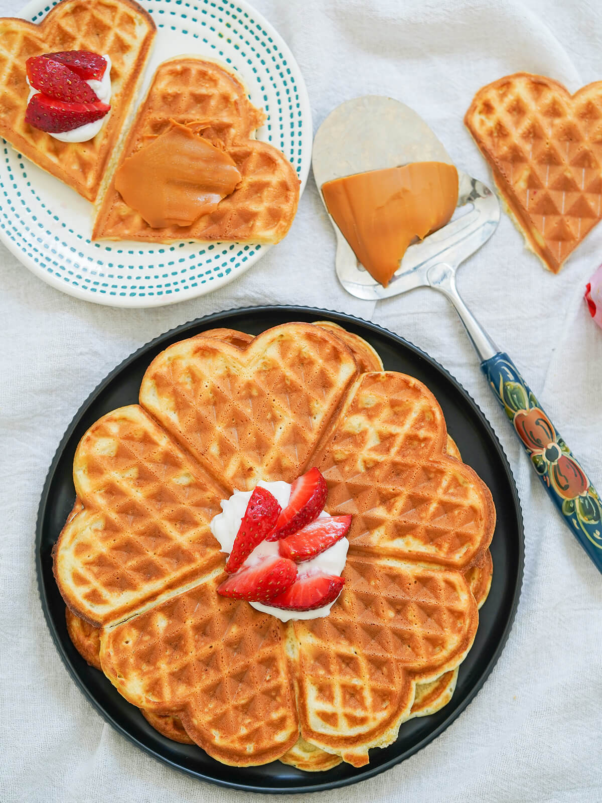 overhead view of a plate of Norwegian waffles with heart-shaped wedges on smaller plate, cheese spar with brown cheese on it to side.