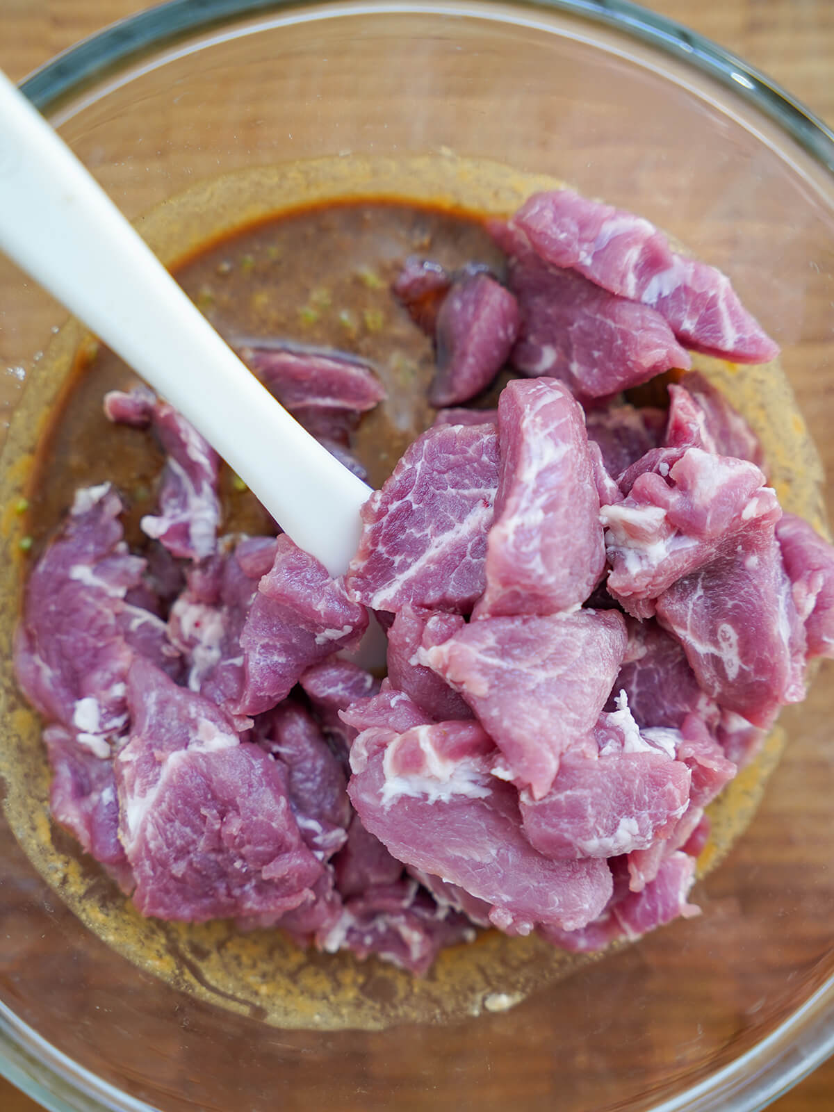 slices of pork in bowl of marinade slices of pork being added to bowl of marinade.