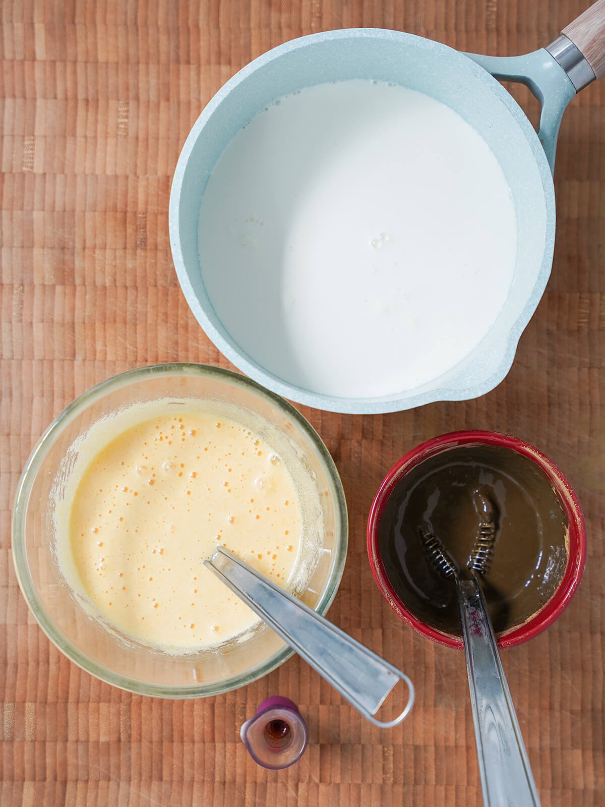 components for hojicha ice cream pot of warm milk, bowl of egg yolks beaten with sugar and small dish with hojicha mixture plus measure of vanilla below.