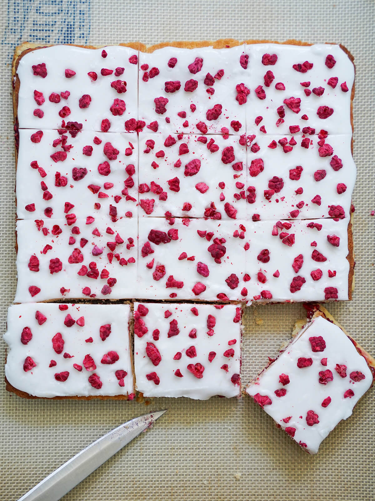 overhead view of block of hindbaersnitter, Danish raspberry bars, with lower section cut into pieces and knife tip below.