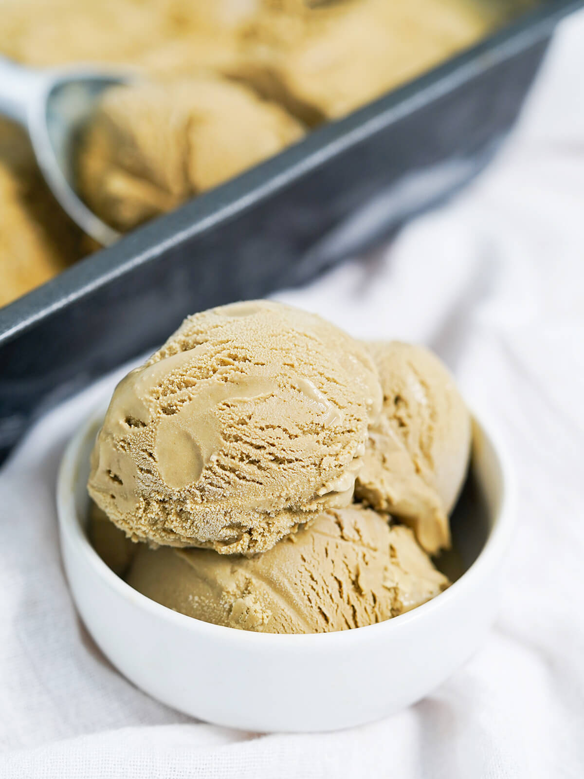 This hojicha ice cream has fantastic depth of flavor and a smooth, creamy texture. It's easier to make than you might think and such a delicious scoop! bowl of hojicha ice cream with dish of more blurred behind.