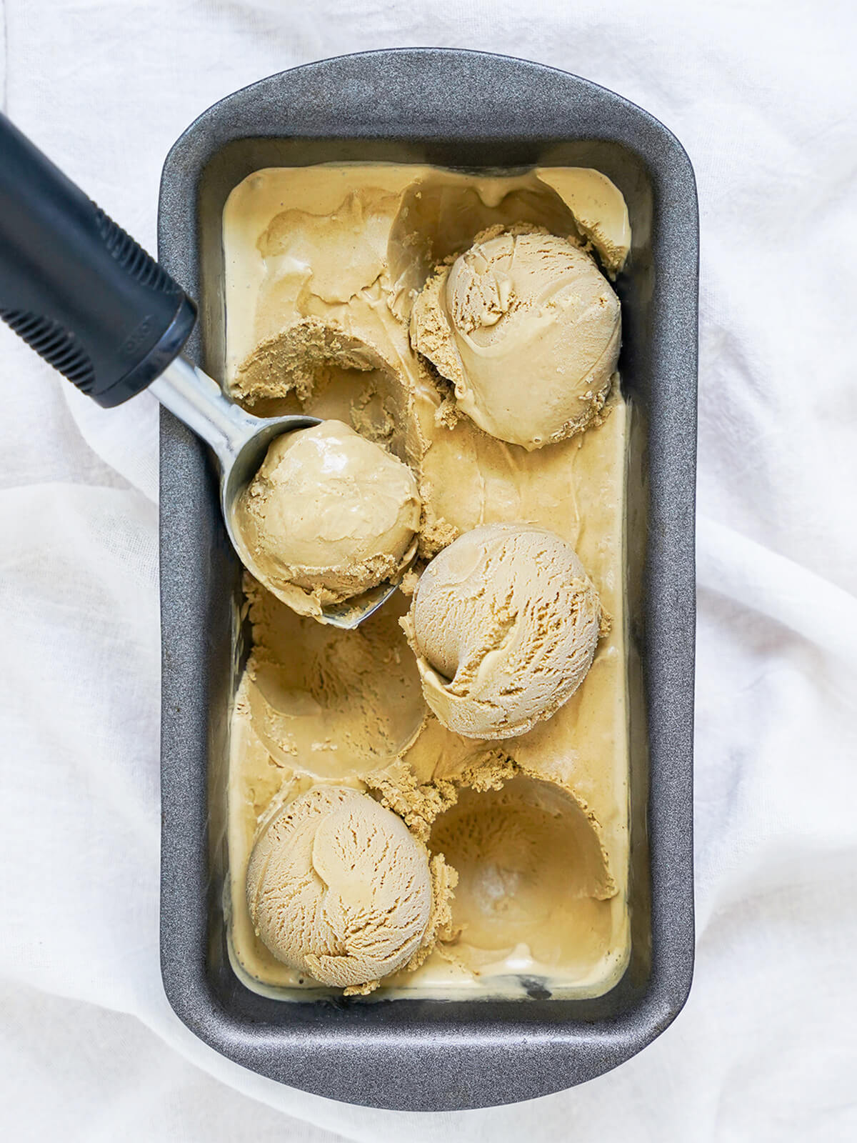 This hojicha ice cream has fantastic depth of flavor and a smooth, creamy texture. It's easier to make than you might think and such a delicious scoop! dish of hojicha ice cream with scoops resting on top and ice cream scoop on one side.