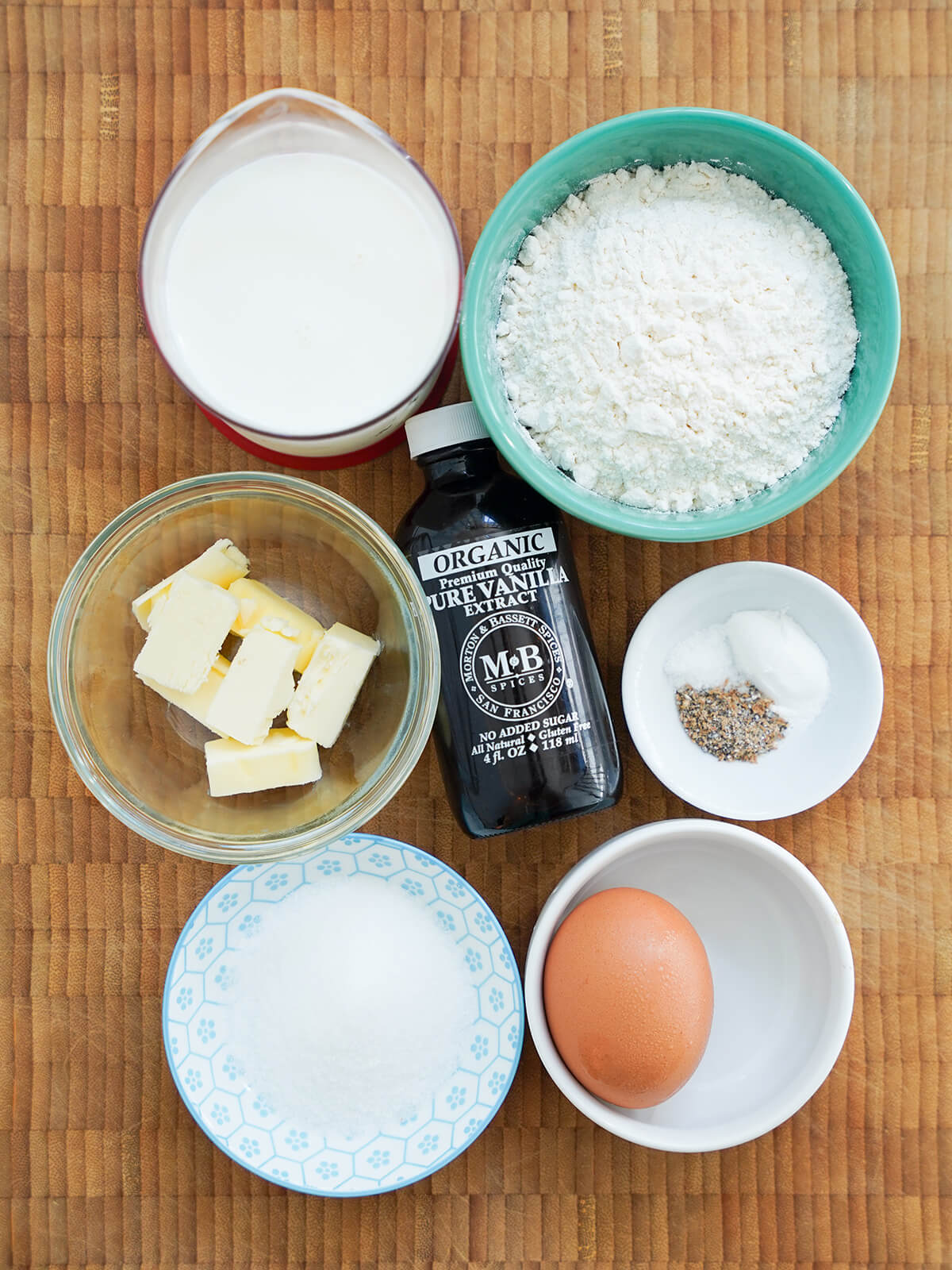 bowls of flour, sugar, butter chunks, egg, measure of milk and bottle of vanilla.