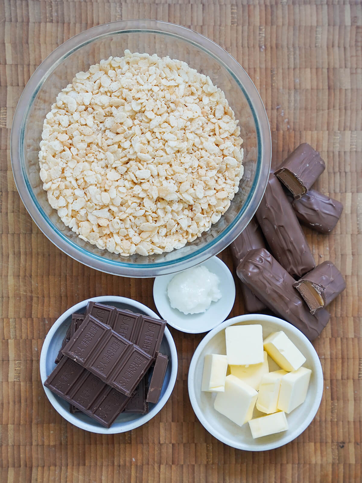 ingredients for mars bar slice bowl of rice krispies, dishes with chocolate, butter and small amount of coconut oil and mars bars aka milky way bars to side.