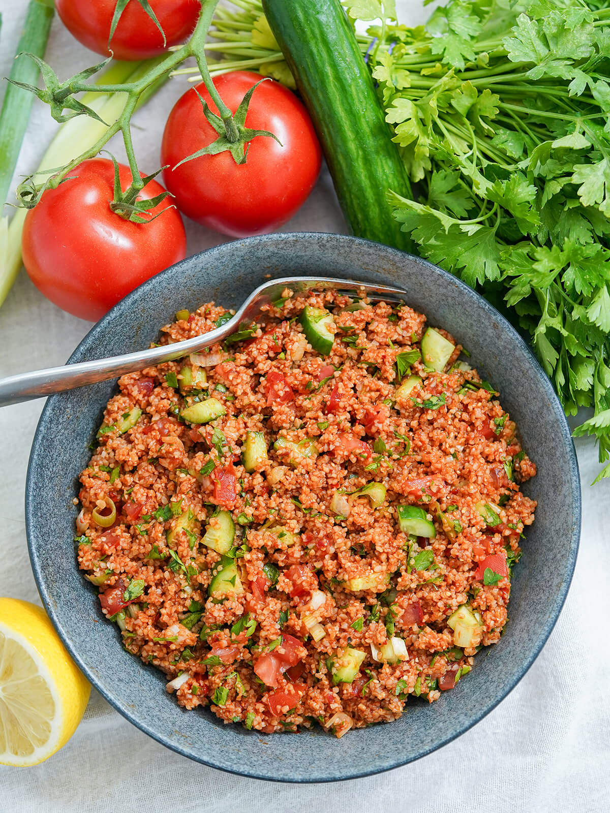 Kisir is a simple, flavor-packed Turkish bulgur salad with wonderful tart-savory flavors. It's easy to make, naturally vegan and perfect as a meze dish, side or pack it for a picnic! overhead view of bowl of kisir Turkish bulgur salad with parsley, cucumber and tomatoes above bowl.