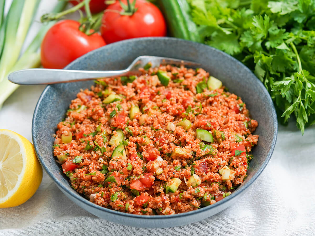 bowl of kisir Turkish bulgur salad side view of bowl of kisir Turkish bulgur salad with fork at back and ingredients around bowl.