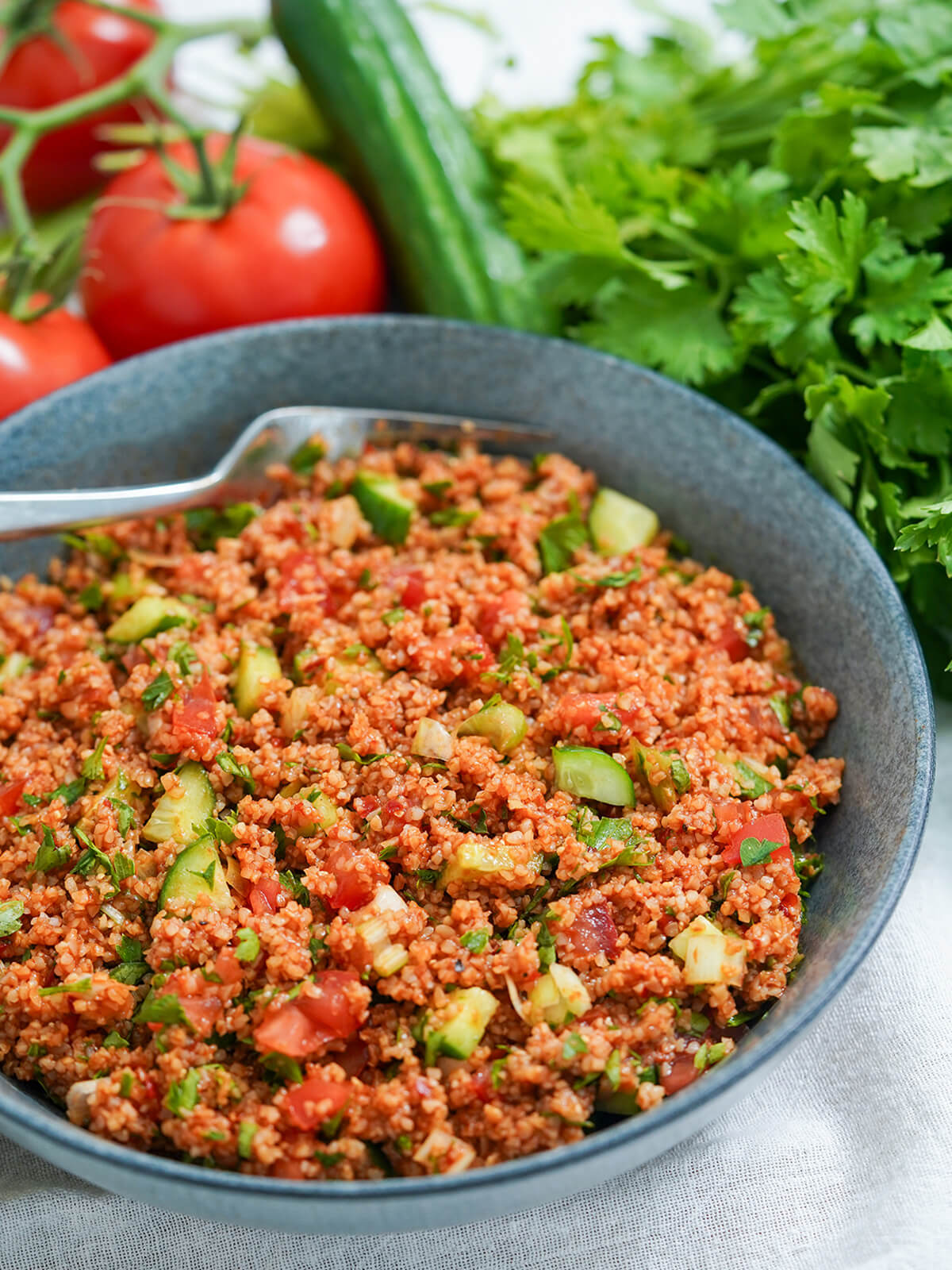Kisir is a simple, flavor-packed Turkish bulgur salad with wonderful tart-savory flavors. It's easy to make, naturally vegan and perfect as a meze dish, side or pack it for a picnic! side view if kisir Turkish bulgur salad with parsley, cucumber and tomatoes in background.