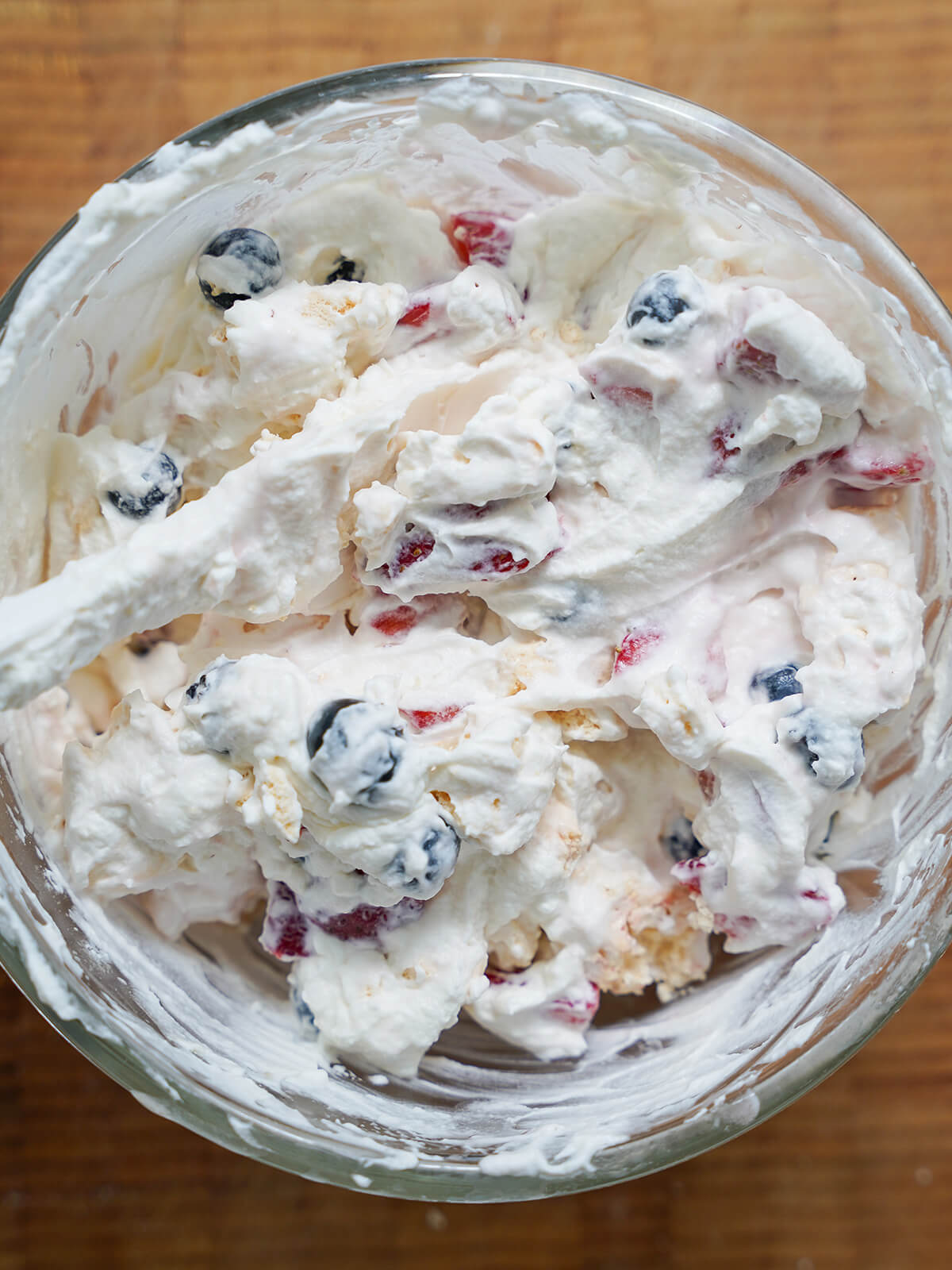 mixing Eton mess bowl with cream, fruit and meringue mixture with spatula in it on top.
