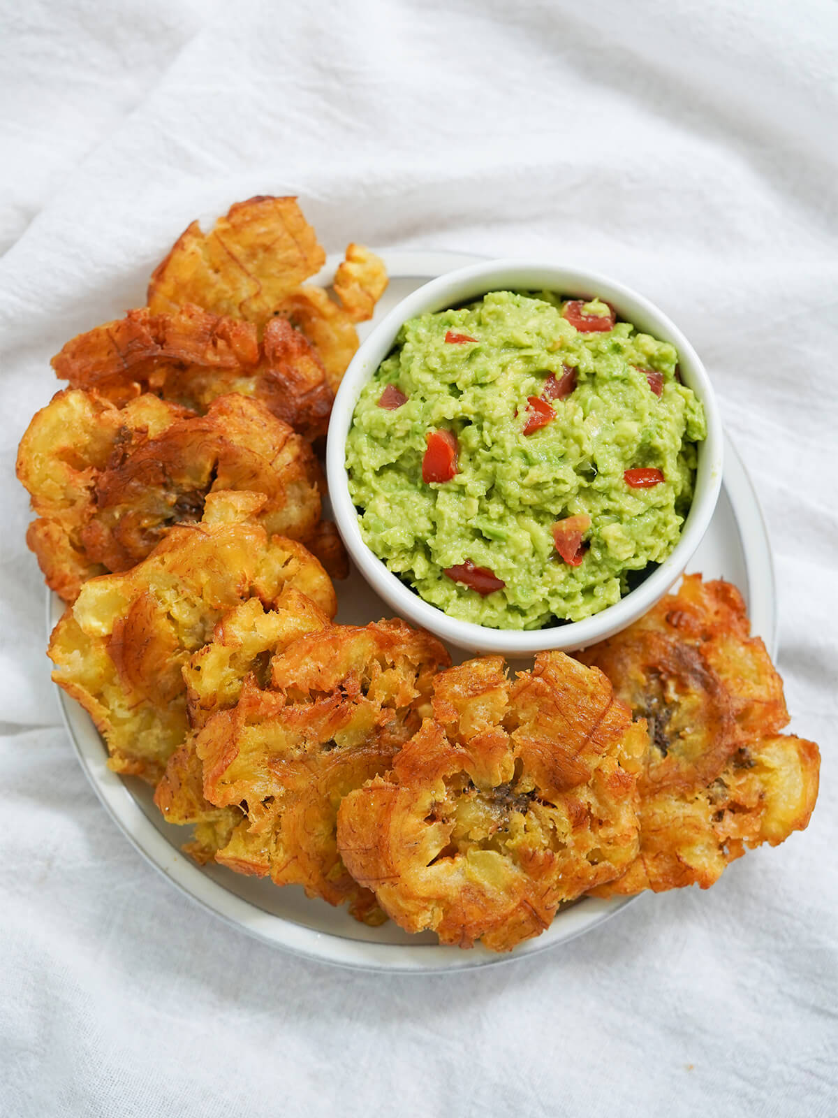 overhead view of a plate of patacones or tostones with small bowl of guacamole on side of plate.