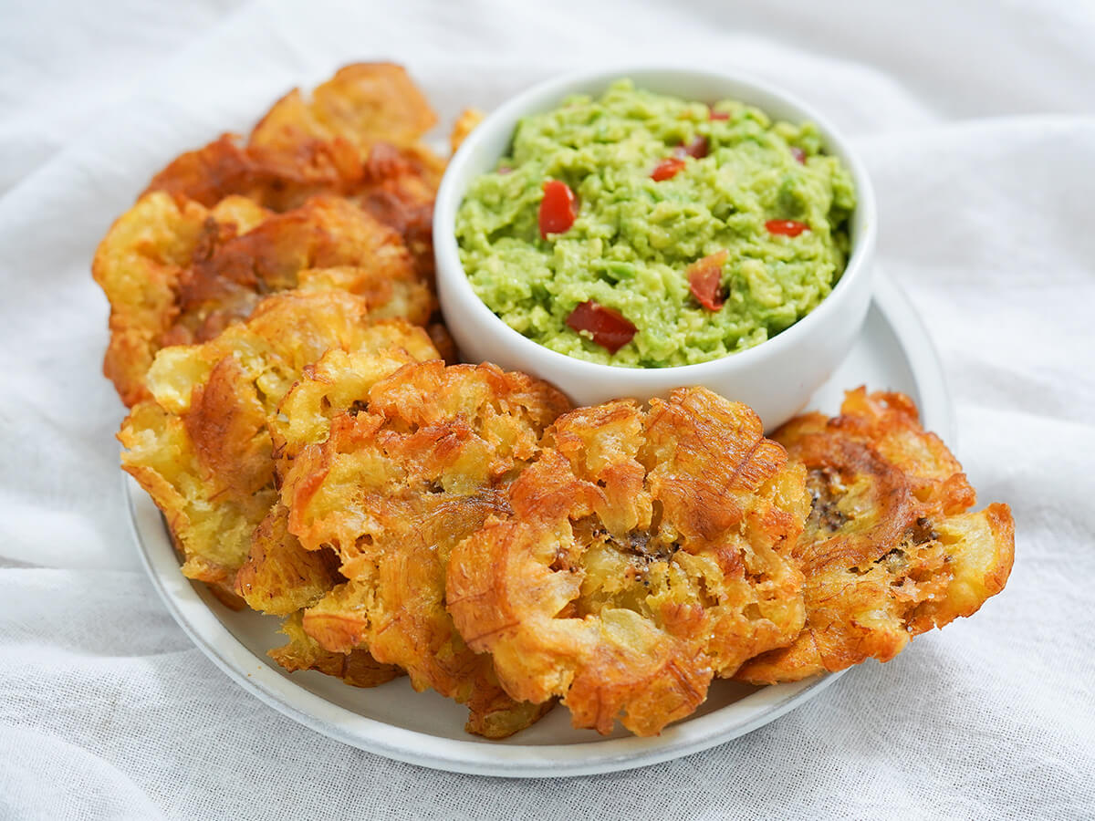 plate of patacones aka tostones with small bowl of guacamole behind.