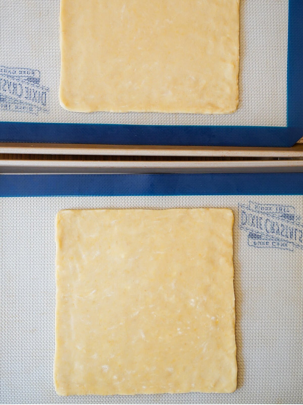 square of cookie dough on lined baking sheet with part view of other above.