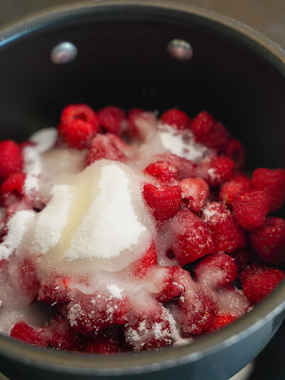 sugar, raspberries and lemon juice in pot starting to make raspberry jam raspberries, sugar in pot with areas moist from lemon juice over the top.