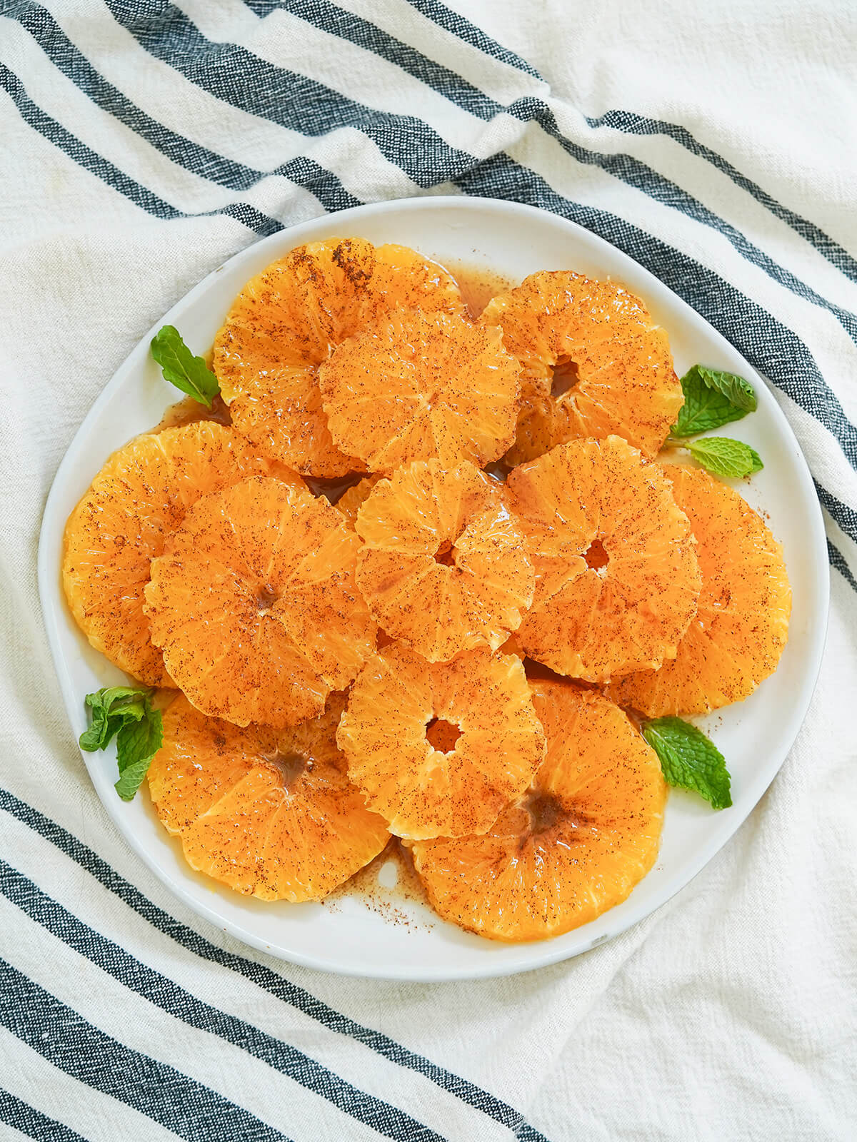 overhead view of a plate of Moroccan oranges with cinnamon garnished with mint on sides.