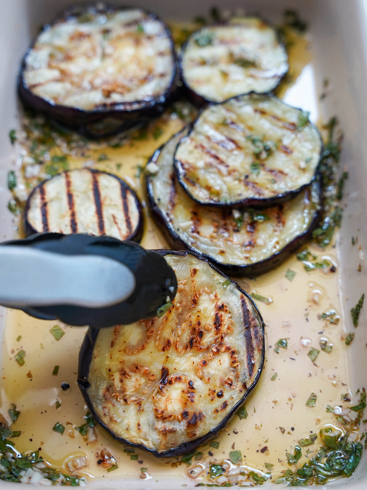 adding a slice of grilled eggplant to marinade mixture in dish with more slices behind.