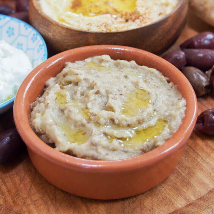 small dish of baba ghanoush, eggplant dip, with part view of other bowls of dips to side and behind.