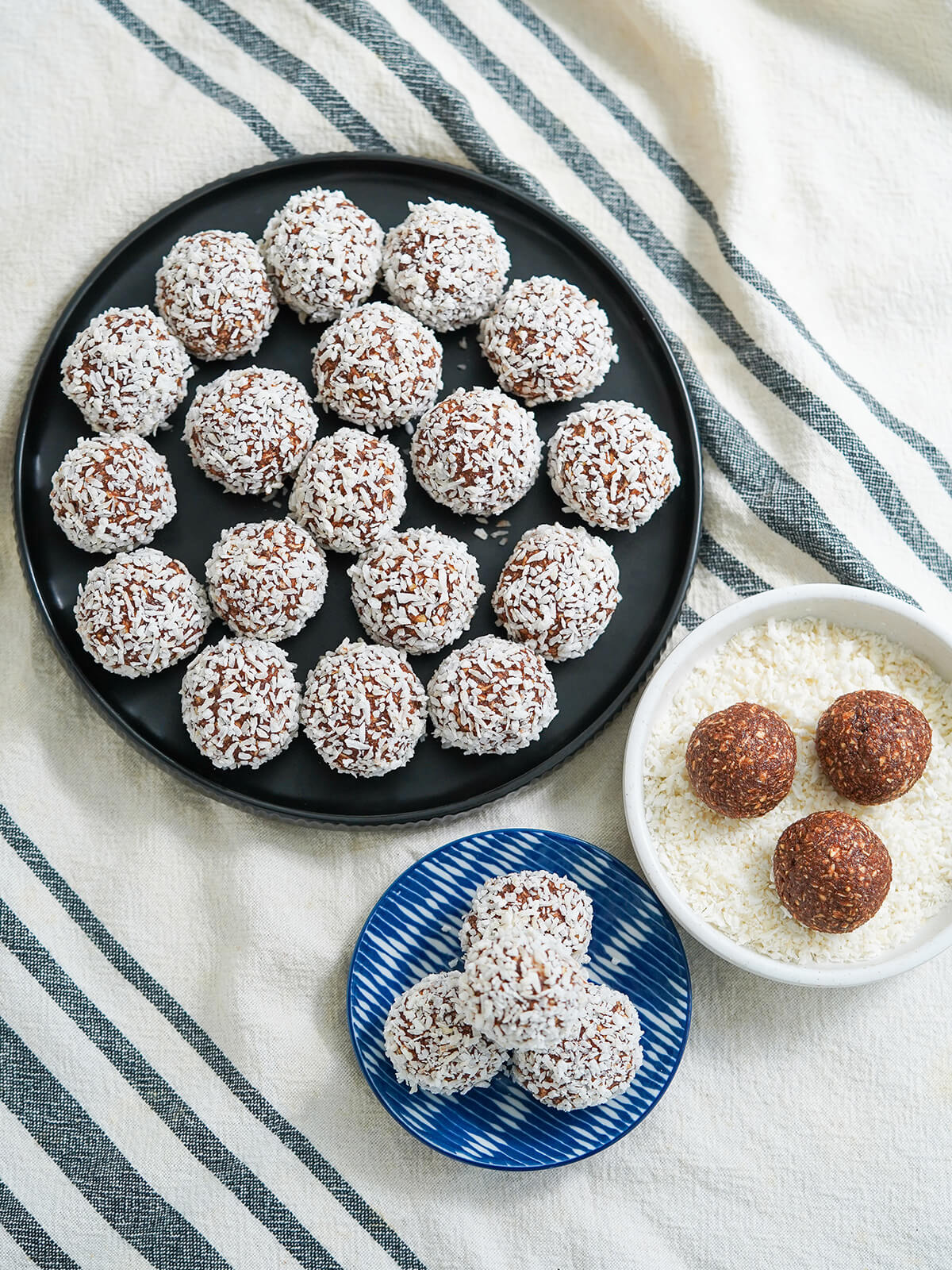 overhead view of large and small plates of chocolate oat balls chokladbollar with some in dish of coconut ready to roll to coat them.